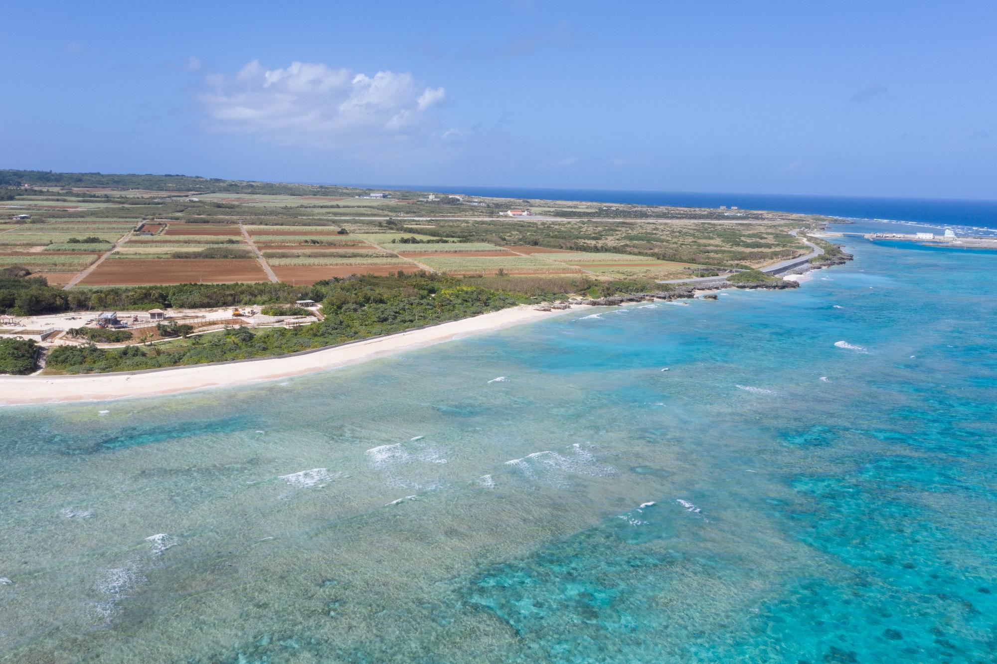 晴れた日に緑色の雑木林に囲まれた白い砂浜が続く長浜ビーチと青い海を上空から撮影した写真