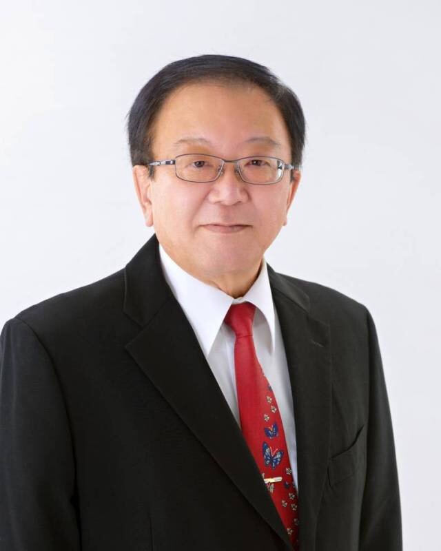黒いスーツで赤いネクタイを付けている粟国村長の高良修一氏の写真